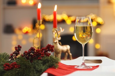 Photo of White wine in glass and Christmas decor on tray against blurred lights, bokeh effect