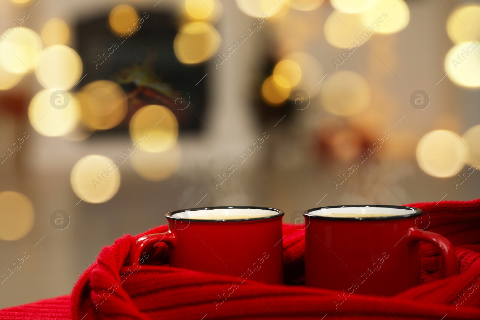 Photo of Tasty cocoa in cups and red scarf against blurred Christmas lights, closeup. Bokeh effect