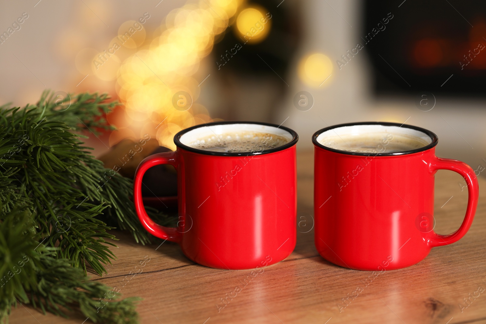 Photo of Tasty cocoa in cups and fir branches on wooden table against blurred Christmas lights, bokeh effect