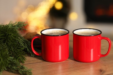 Photo of Tasty cocoa in cups and fir branches on wooden table against blurred Christmas lights, bokeh effect