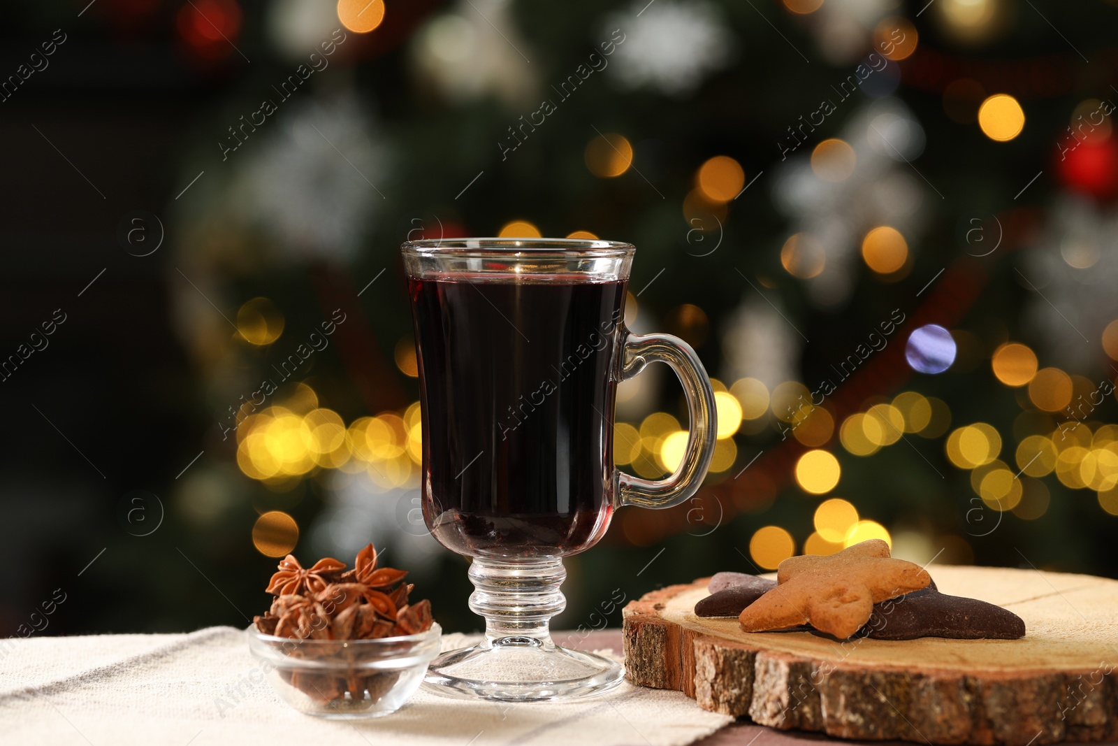 Photo of Aromatic mulled wine in glass cup, cookies and anise stars on table against blurred Christmas lights, bokeh effect