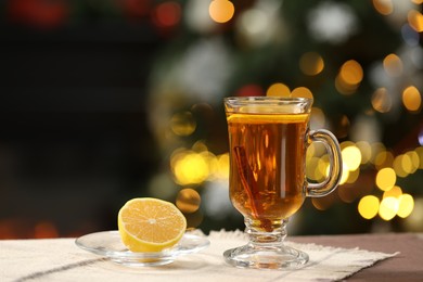 Photo of Hot tea with lemon and cinnamon on table against blurred Christmas lights, bokeh effect