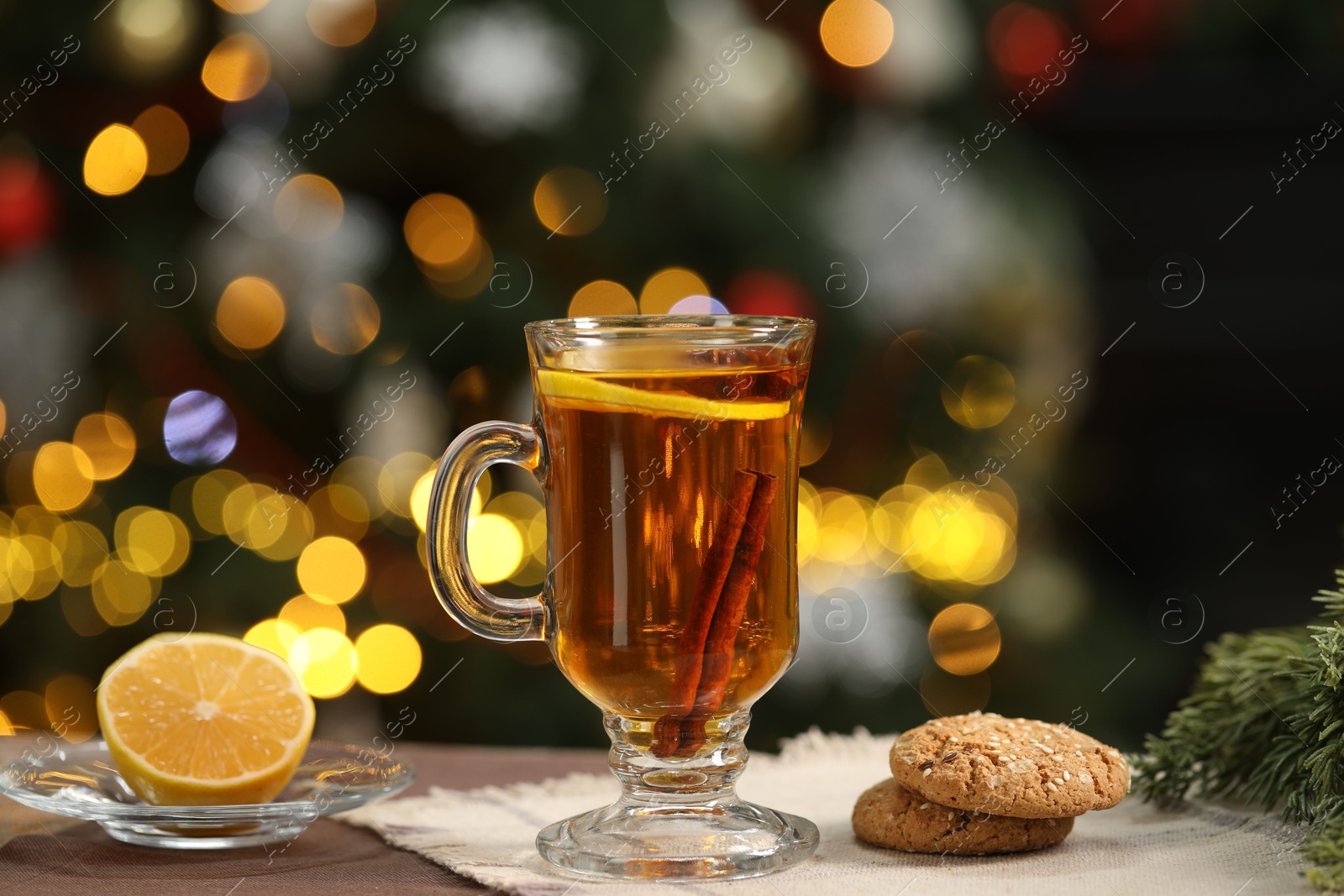 Photo of Hot tea with lemon, cinnamon and tasty cookies on table against blurred Christmas lights, bokeh effect