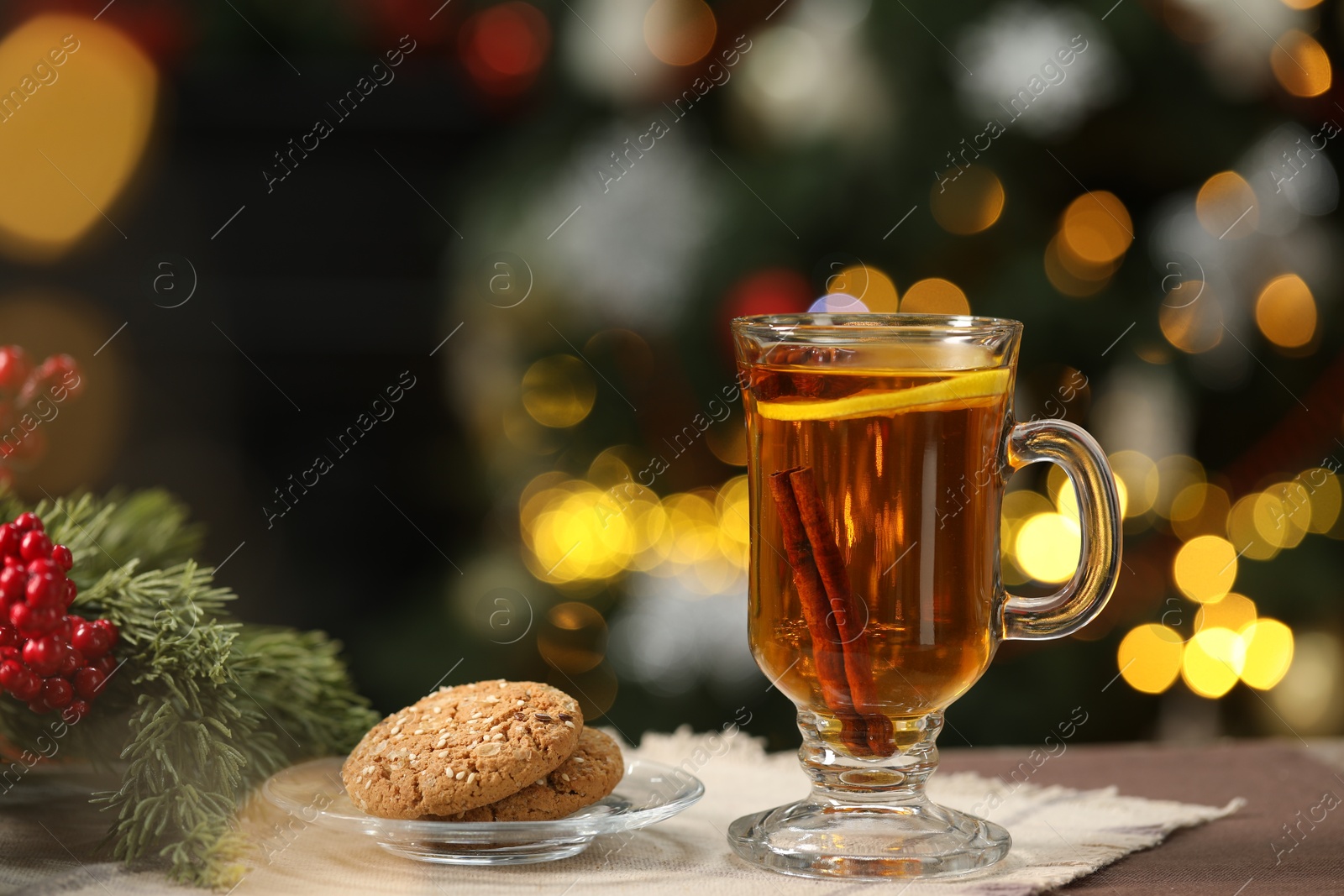 Photo of Hot tea with lemon, cinnamon and tasty cookies on table against blurred Christmas lights, bokeh effect