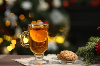 Hot tea with lemon and tasty cookies on table against blurred Christmas lights, bokeh effect