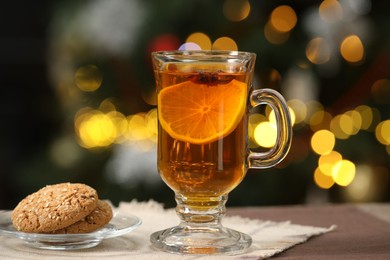 Photo of Hot tea with lemon and tasty cookies on table against blurred Christmas lights, bokeh effect