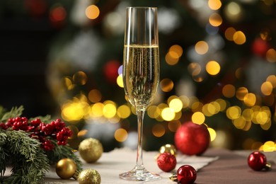 Photo of Champagne in glass and decor on table against blurred Christmas lights, bokeh effect