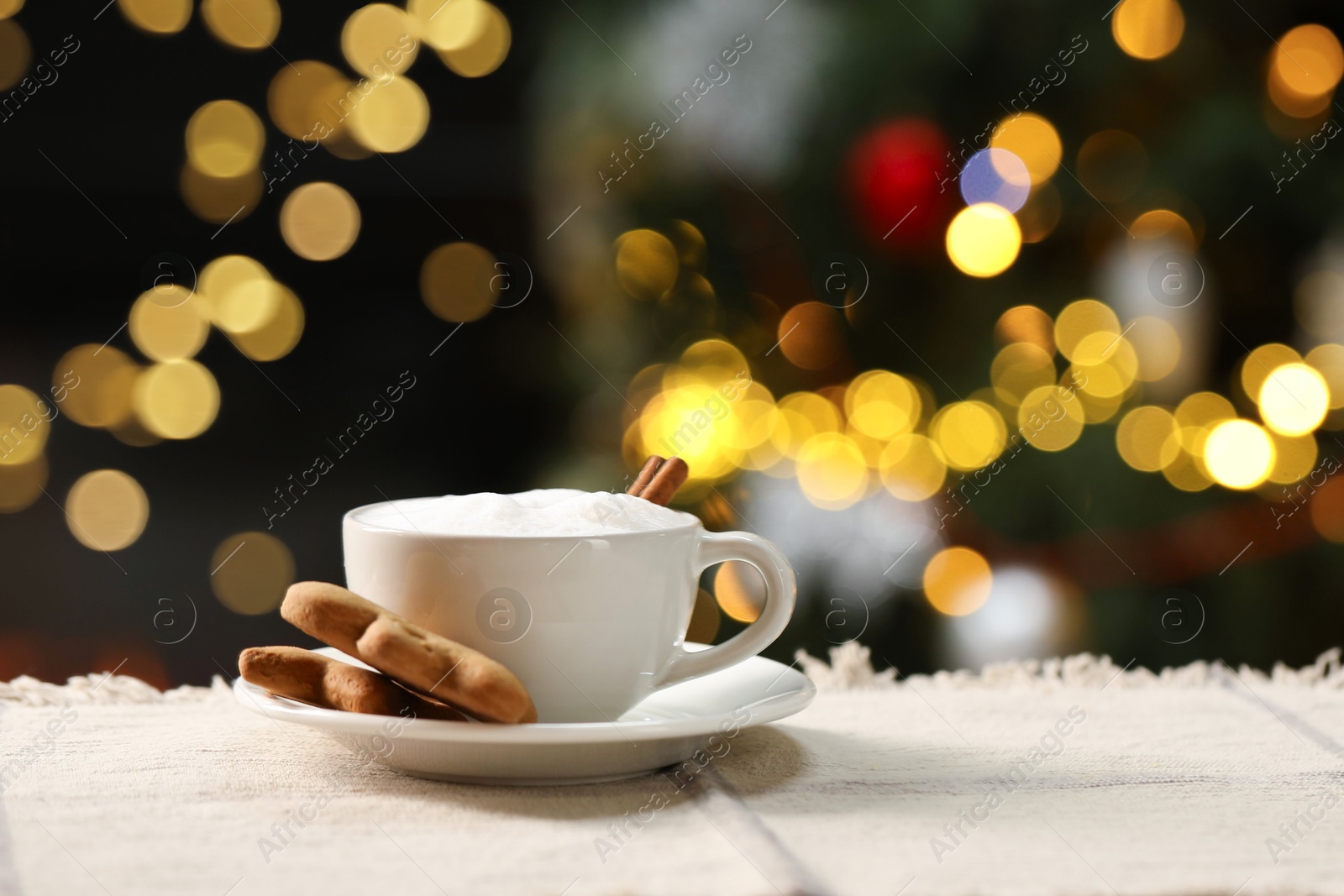 Photo of Aromatic coffee in cup and tasty cookies on table against blurred Christmas lights, space for text. Bokeh effect