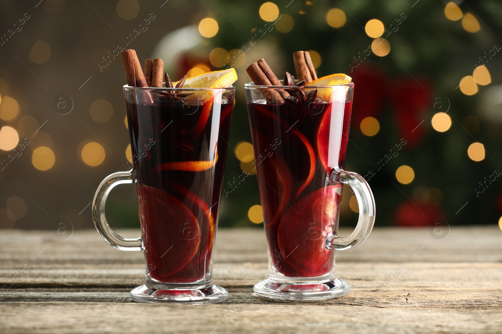 Photo of Tasty mulled wine with spices on wooden table against blurred Christmas lights, bokeh effect