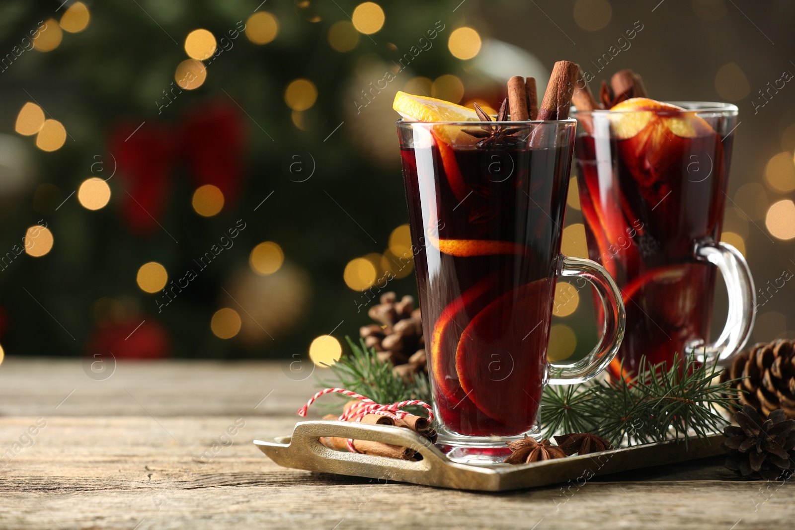 Photo of Tasty mulled wine with spices and decor on wooden table against blurred Christmas lights, space for text. Bokeh effect