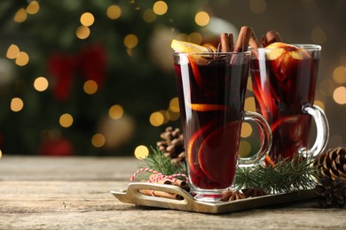 Photo of Tasty mulled wine with spices and decor on wooden table against blurred Christmas lights, space for text. Bokeh effect