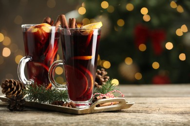 Photo of Tasty mulled wine with spices and decor on wooden table against blurred Christmas lights, space for text. Bokeh effect