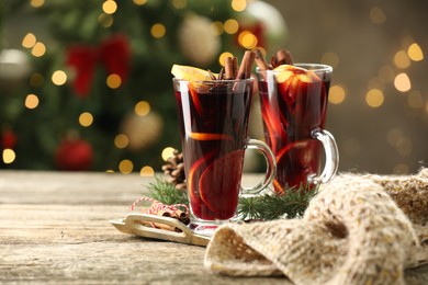 Photo of Tasty mulled wine with spices and decor on wooden table against blurred Christmas lights, space for text. Bokeh effect