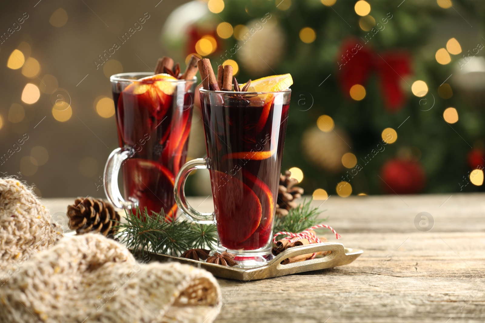 Photo of Tasty mulled wine with spices and decor on wooden table against blurred Christmas lights, space for text. Bokeh effect