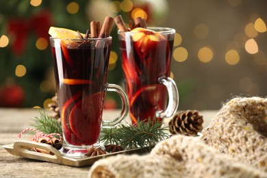 Photo of Tasty mulled wine with spices and decor on wooden table against blurred Christmas lights, bokeh effect