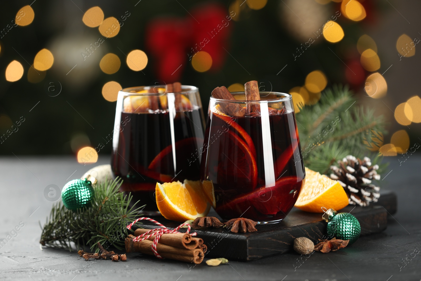 Photo of Tasty mulled wine with spices and decor on grey table against blurred Christmas lights, bokeh effect