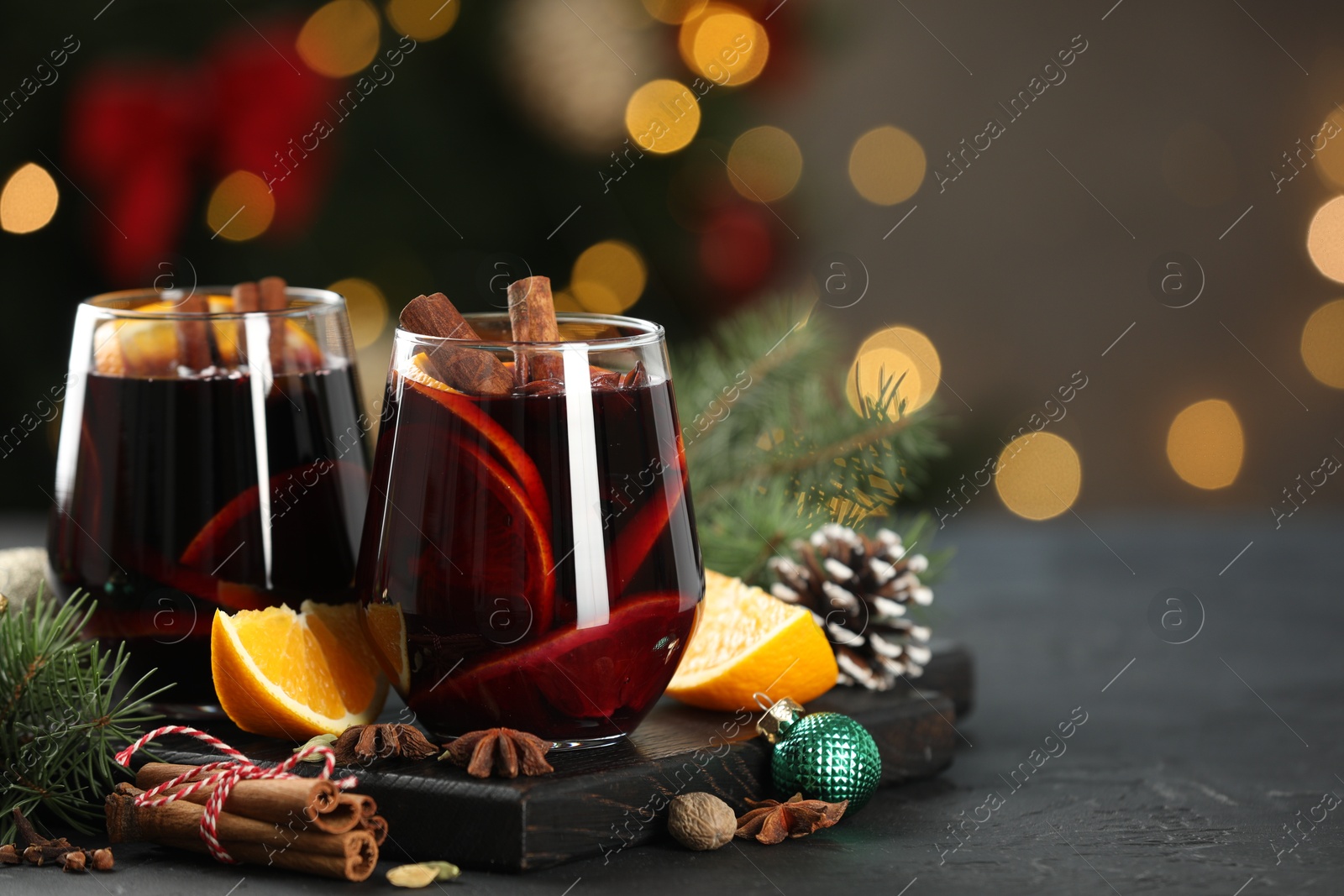 Photo of Tasty mulled wine with spices and decor on grey table against blurred Christmas lights, space for text. Bokeh effect