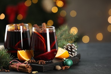 Photo of Tasty mulled wine with spices and decor on grey table against blurred Christmas lights, space for text. Bokeh effect