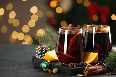 Photo of Tasty mulled wine with spices and decor on grey table against blurred Christmas lights, space for text. Bokeh effect