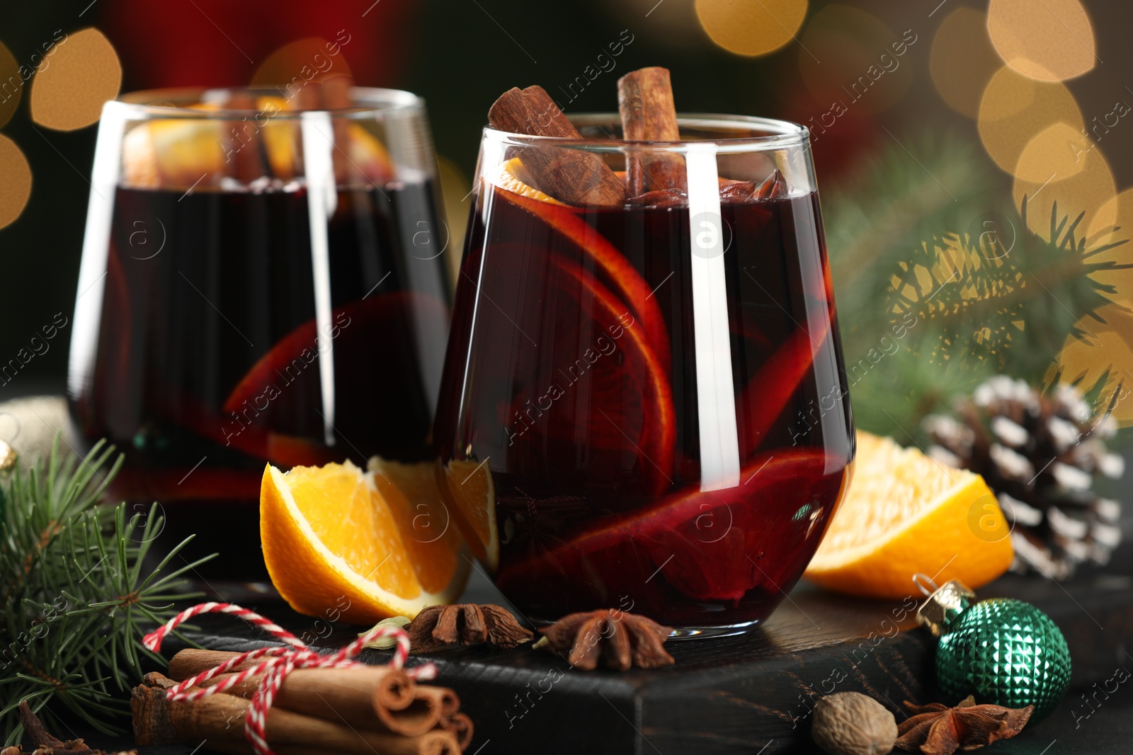 Photo of Tasty mulled wine with spices and decor on table against blurred Christmas lights, closeup. Bokeh effect