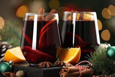 Photo of Tasty mulled wine with spices and decor on table against blurred Christmas lights, closeup. Bokeh effect