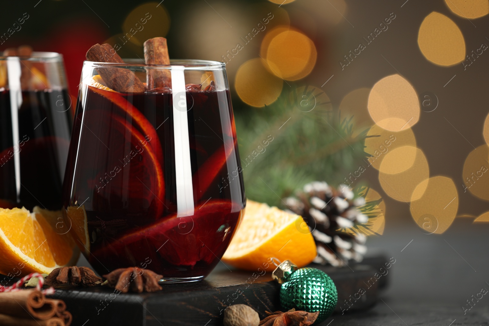 Photo of Tasty mulled wine with spices and decor on table against blurred Christmas lights, closeup. Bokeh effect