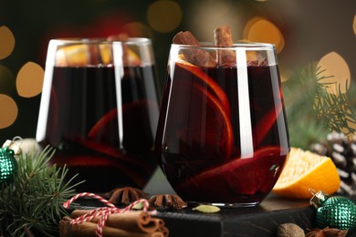 Photo of Tasty mulled wine with spices and decor on table against blurred Christmas lights, closeup. Bokeh effect