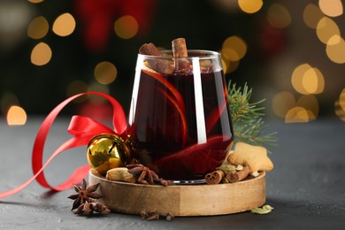 Photo of Tasty mulled wine with spices, cookies and decor on grey table against blurred Christmas lights, closeup. Bokeh effect