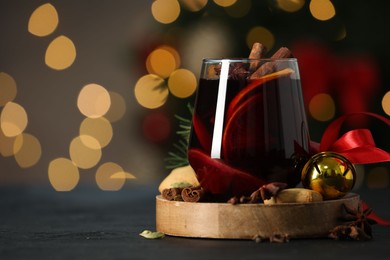 Photo of Tasty mulled wine with spices, cookie and decor on grey table against blurred Christmas lights, space for text. Bokeh effect