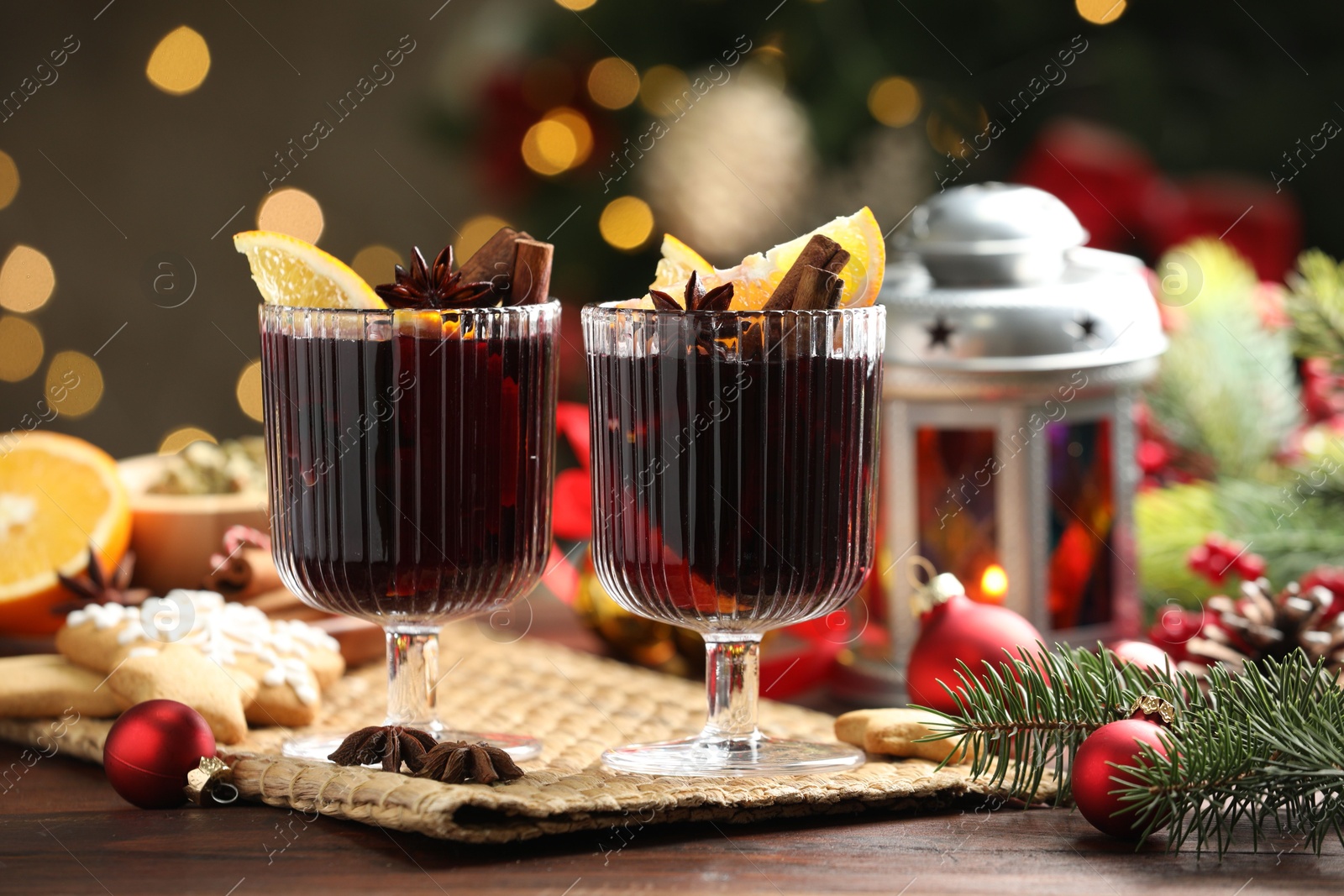 Photo of Tasty mulled wine with spices, cookies and decor on wooden table against blurred Christmas lights, bokeh effect