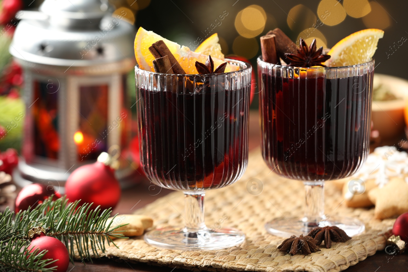 Photo of Tasty mulled wine with spices, cookies and decor on table against blurred Christmas lights, closeup. Bokeh effect