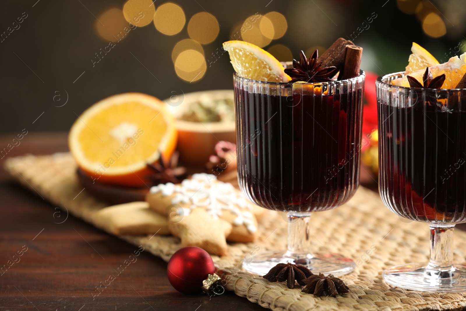 Photo of Tasty mulled wine with spices, cookies and decor on wooden table against blurred Christmas lights, closeup. Bokeh effect