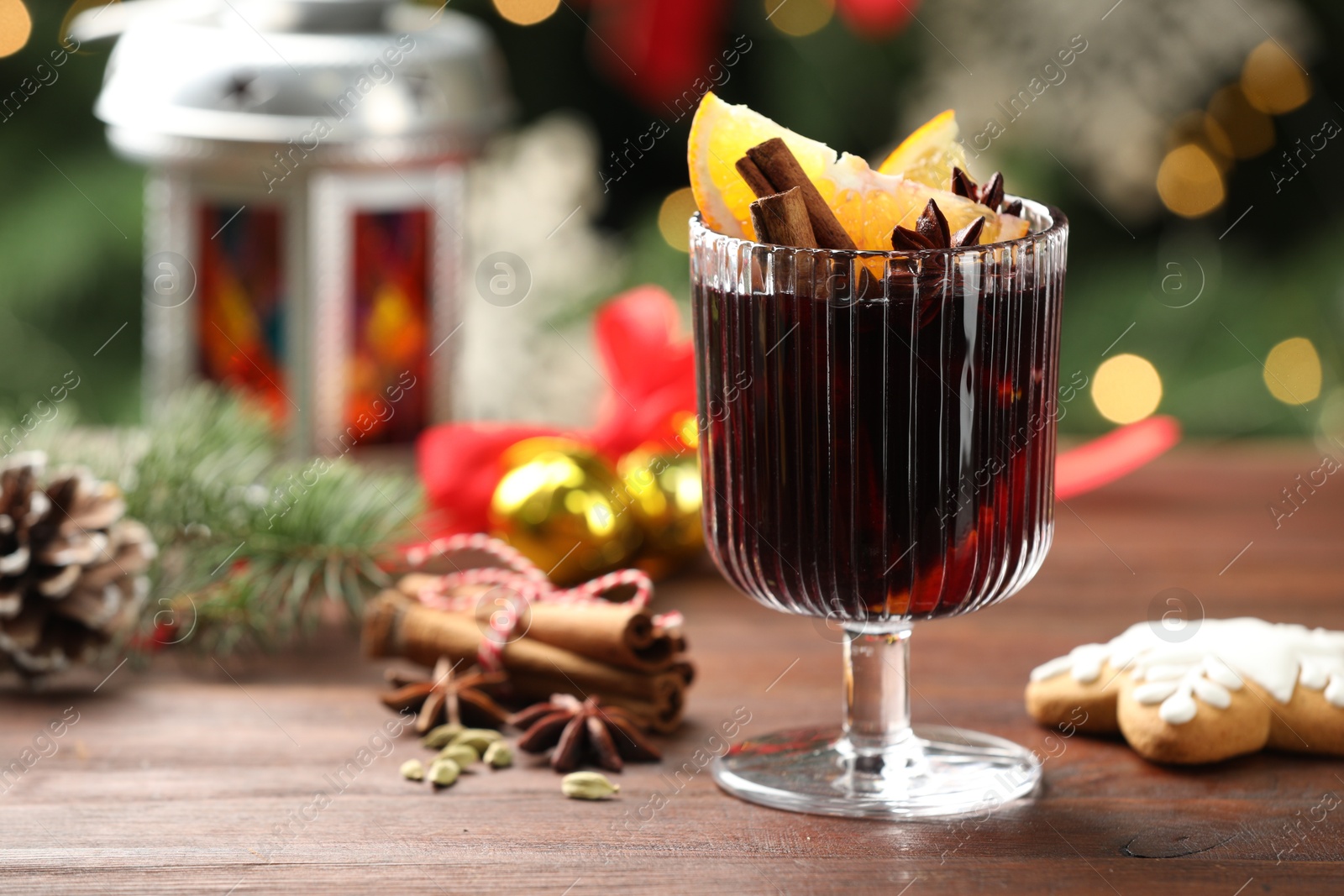 Photo of Tasty mulled wine with spices and decor on wooden table against blurred Christmas lights, closeup. Bokeh effect