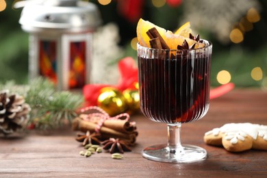 Photo of Tasty mulled wine with spices and decor on wooden table against blurred Christmas lights, closeup. Bokeh effect