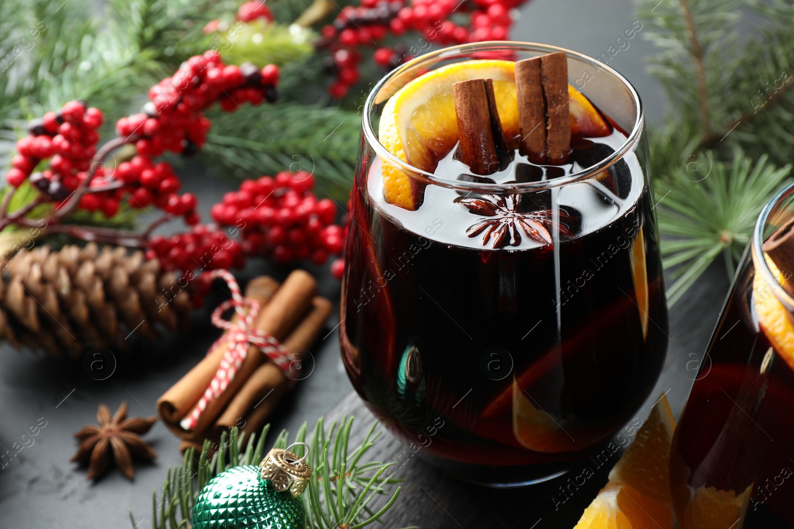 Photo of Tasty mulled wine with spices and Christmas decor on black table, closeup