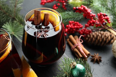 Photo of Tasty mulled wine with spices and Christmas decor on black table, closeup