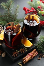 Photo of Tasty mulled wine with spices and Christmas decor on black table, closeup