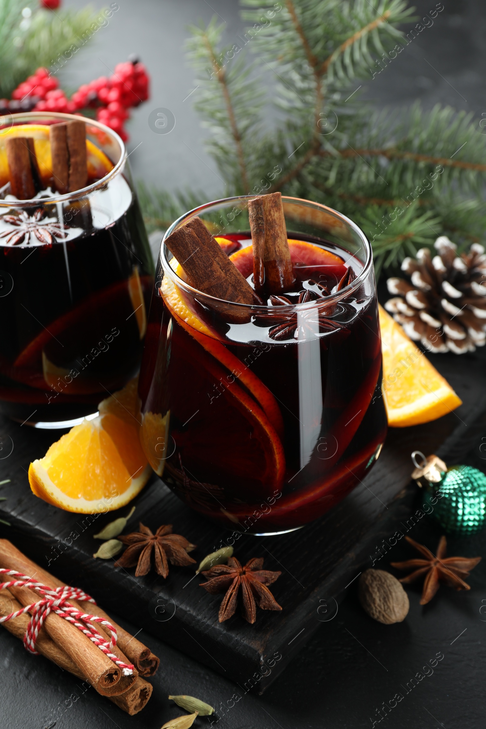 Photo of Tasty mulled wine with spices and Christmas decor on black table, closeup