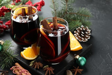 Photo of Tasty mulled wine with spices and Christmas decor on black table, closeup