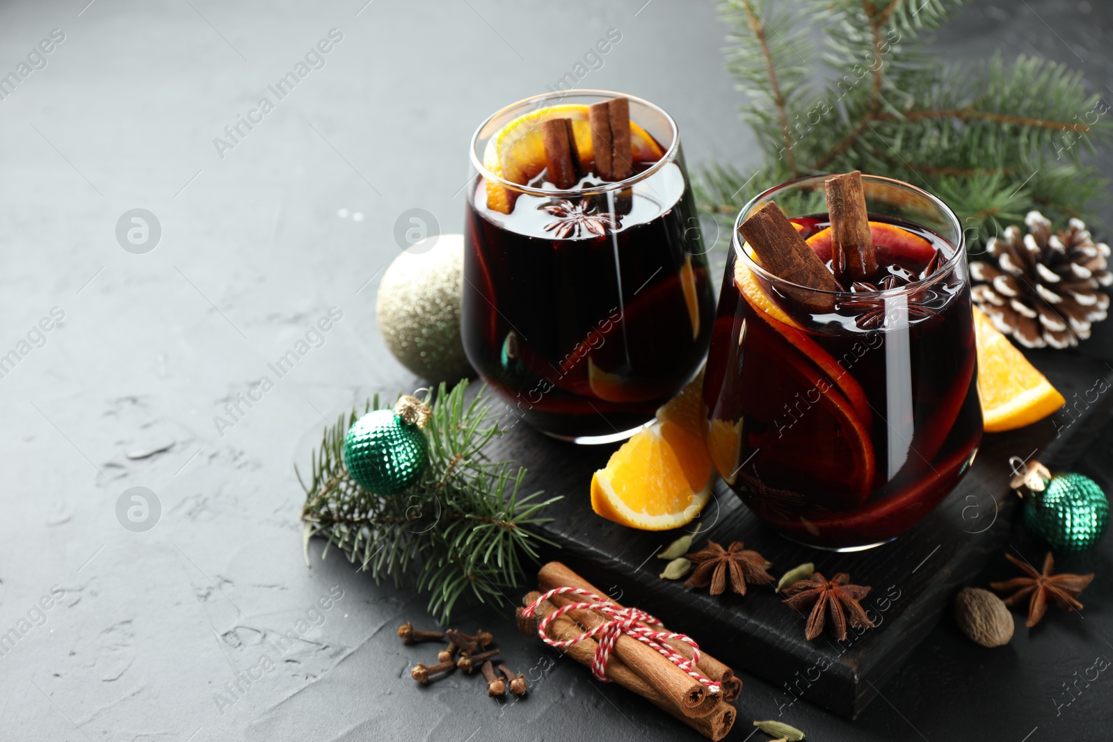 Photo of Tasty mulled wine with spices and Christmas decor on black table, closeup. Space for text