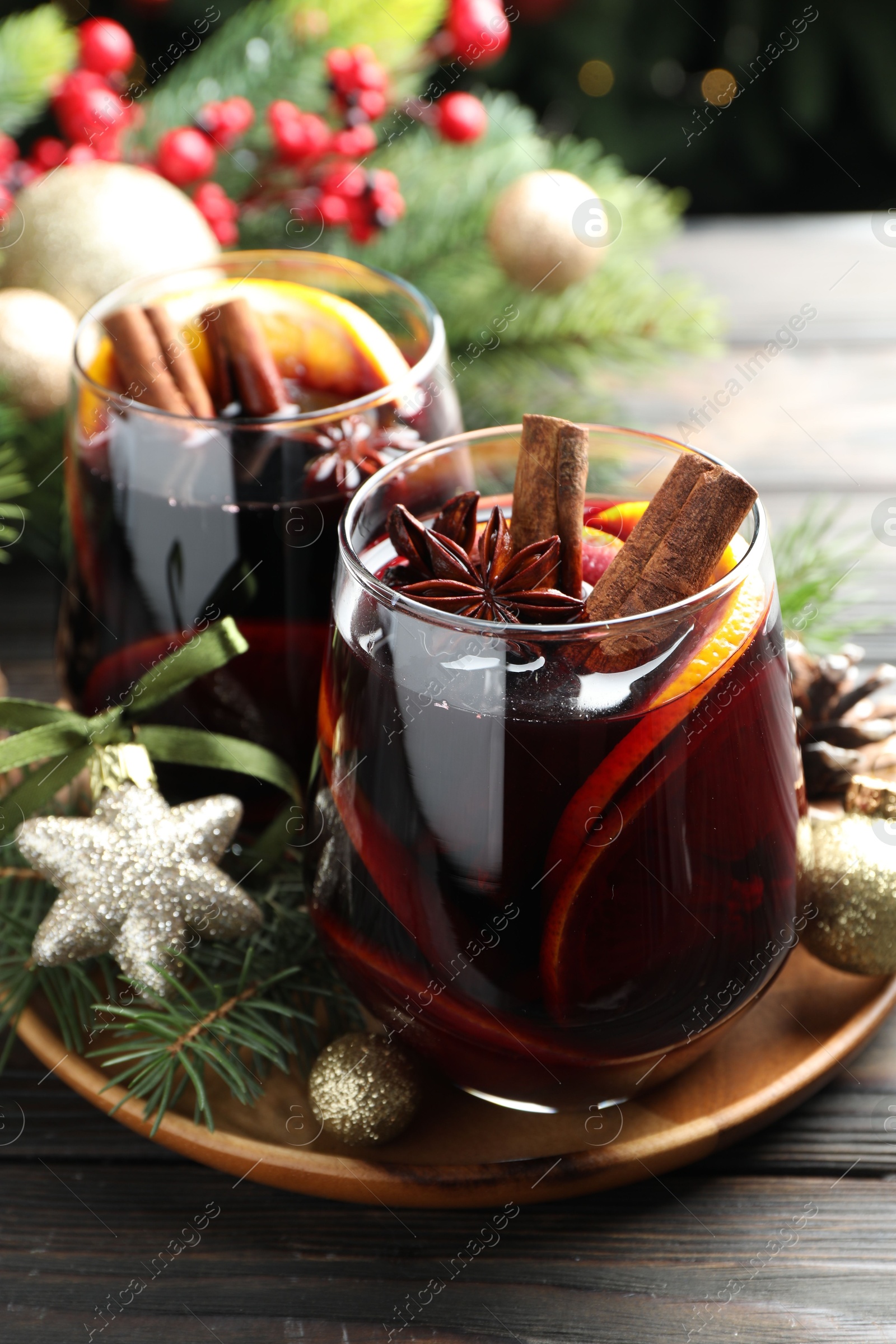 Photo of Tasty mulled wine with spices and Christmas decor on wooden table, closeup