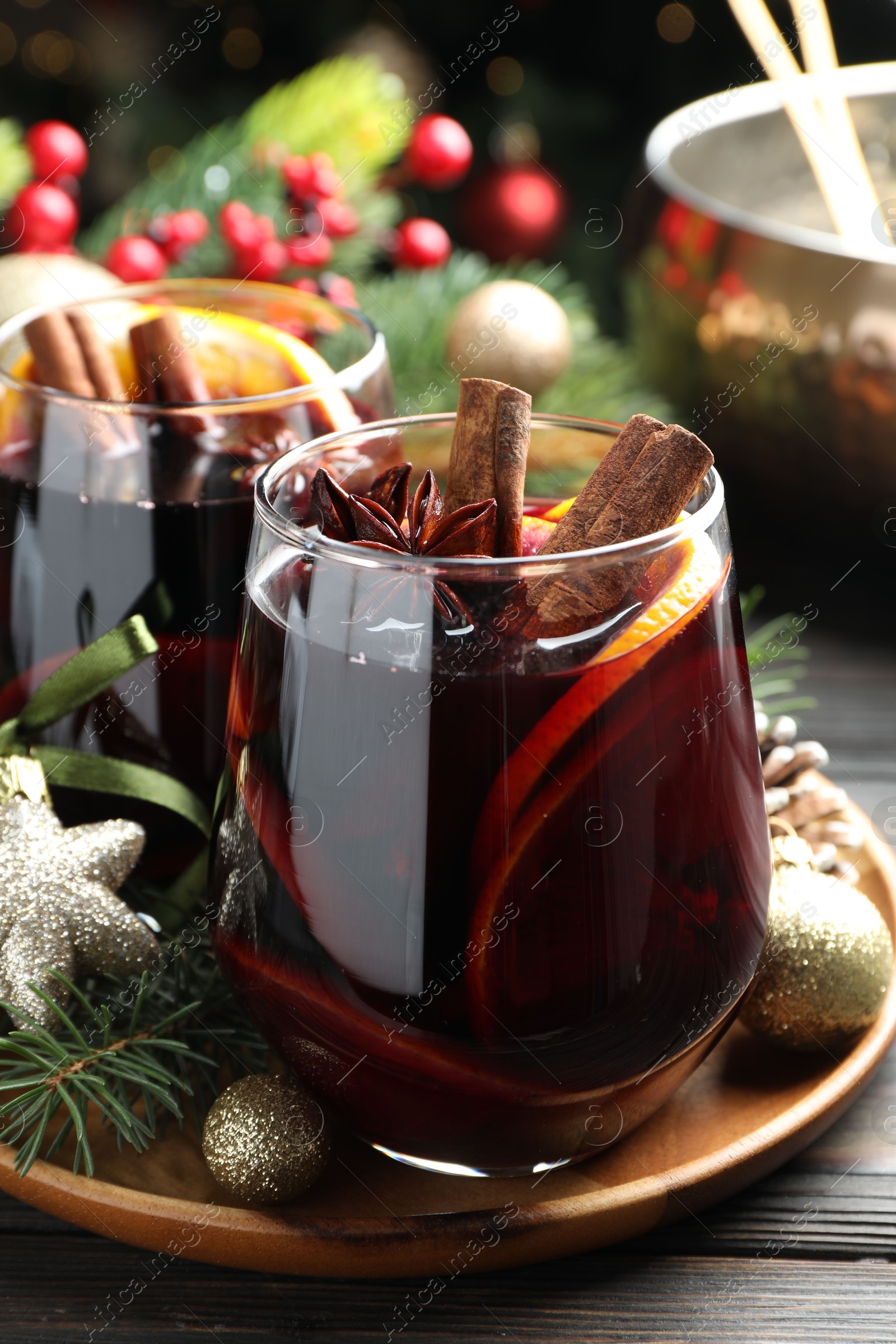 Photo of Tasty mulled wine with spices and Christmas decor on wooden table, closeup