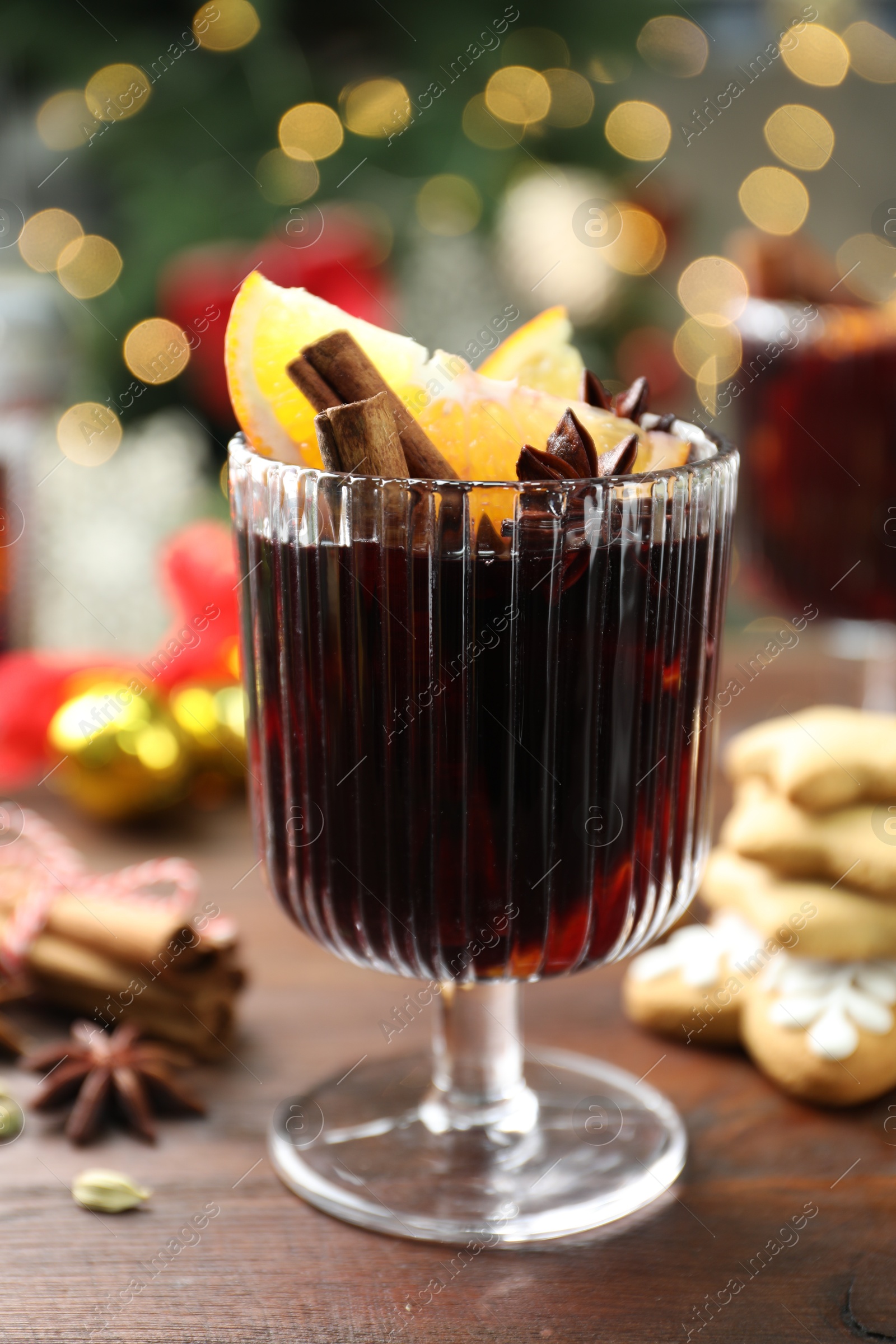 Photo of Tasty mulled wine with spices on wooden table against blurred Christmas lights, closeup. Bokeh effect