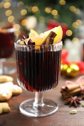 Photo of Tasty mulled wine with spices on wooden table against blurred Christmas lights, closeup. Bokeh effect