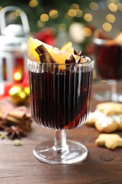 Photo of Tasty mulled wine with spices on wooden table against blurred Christmas lights, closeup. Bokeh effect