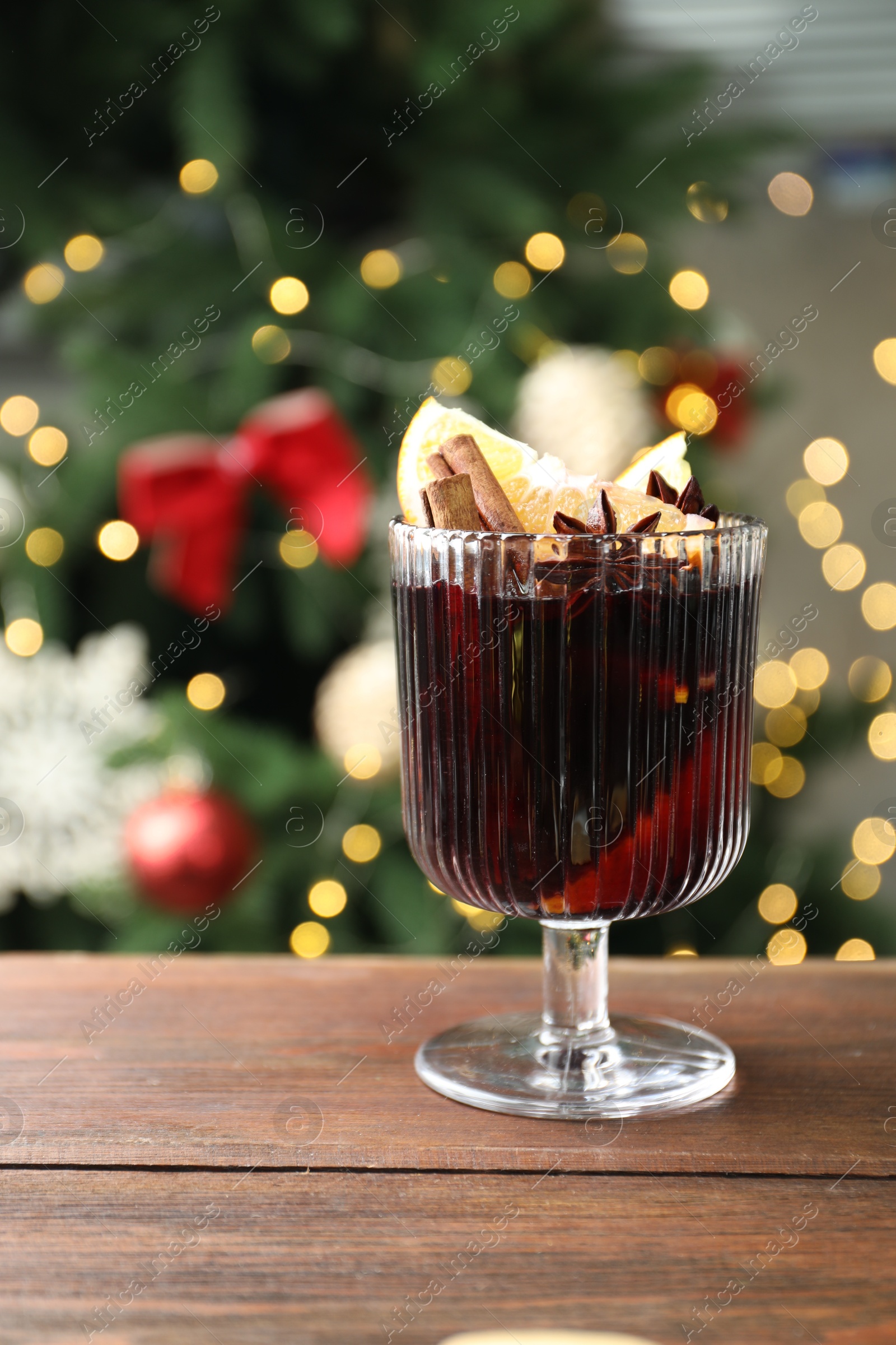 Photo of Tasty mulled wine with spices on wooden table against blurred Christmas lights, space for text. Bokeh effect