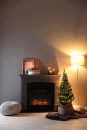 Photo of Small spruce tree in basket decorated with Christmas lights near fireplace indoors