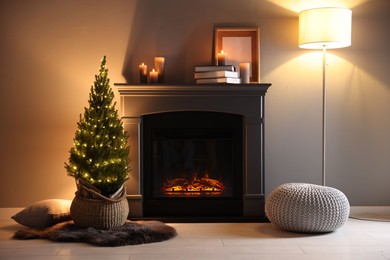 Photo of Small spruce tree in basket decorated with Christmas lights near fireplace indoors