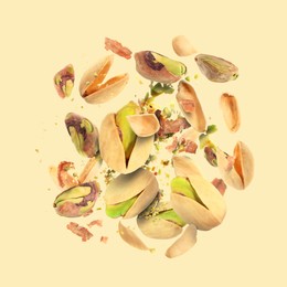 Image of Tasty pistachios with cracked nutshell in air on beige background