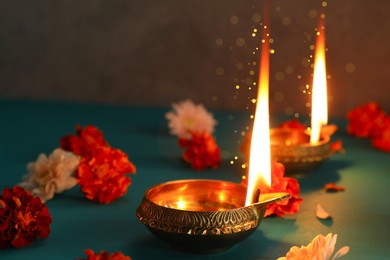 Image of Happy Diwali celebration. Diya lamps burning and beautiful flowers on teal table, closeup. Bokeh effect